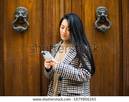 Stock photo of a young asian woman using her cellphone outdoors chatting.
