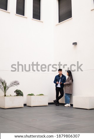 Stock photo of a young couple standing against a white wall using cellphone and talking shot from above.