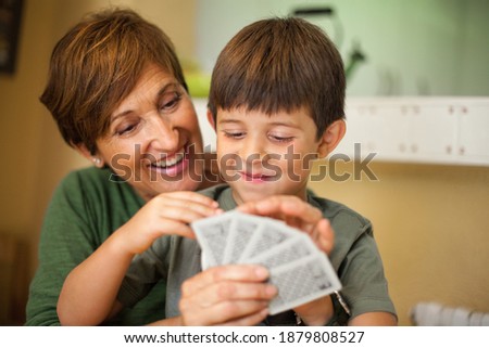 Adorable smiling couple of boy and his grandmother sitting together and smiling while they are playing a cards game. Spending quality leisure time with children and family concept. Royalty-Free Stock Photo #1879808527