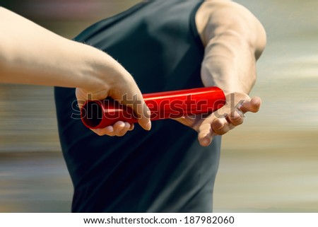 Female relay runner hands over the red pole to male runner Royalty-Free Stock Photo #187982060