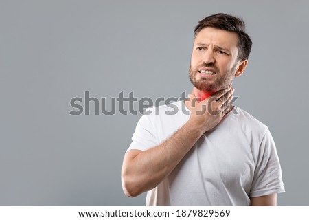 Middle aged sick man having sore throat, looking at copy space over grey studio background. Bearded man touching his red neck, suffering from throat disorder, tonsillitis, throat cancer, cold Royalty-Free Stock Photo #1879829569