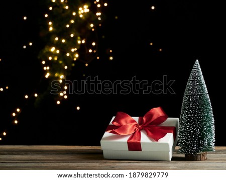 Christmas gift box with fir tree on wooden table against blurred festive lights on dark background, space for text