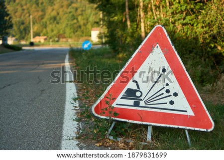 Traffic sign red triangle with car depicting possible loose rocks and gravel road up ahead                              Royalty-Free Stock Photo #1879831699