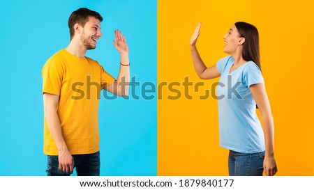 Side view profile portrait of smiling young man and woman waving to each other or giving high five standing isolated on halved yellow and blue studio background, greeting each other Royalty-Free Stock Photo #1879840177