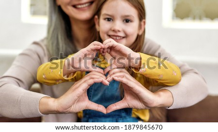 Spreading love. Close up portrait of little girl granddaughter spending time together with her loving granny. They are smiling and showing heart sign. Front view. Selective focus on hands