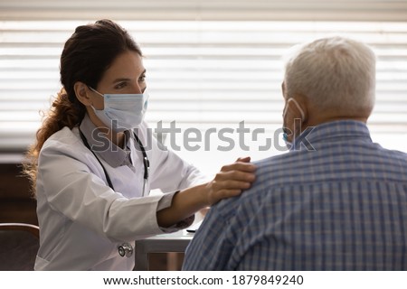Caring female nurse in medical facemask touch calm support elderly male patient in hospital. Supportive woman doctor in facial mask show empathy comfort mature man in clinic. Healthcare concept. Royalty-Free Stock Photo #1879849240