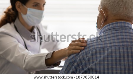 Close up view of caring female doctor in facial mask touch support elderly patient. Supportive woman GP or nurse in protective facemask comfort unhealthy elderly man at consultation. Corona concept. Royalty-Free Stock Photo #1879850014