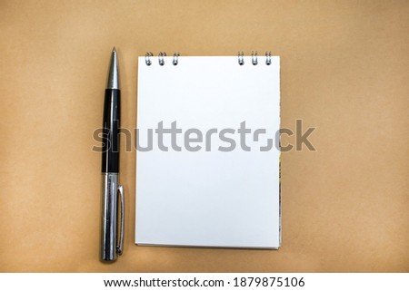 On a brown background is a notebook with a white sheet and a pen. Concept photo