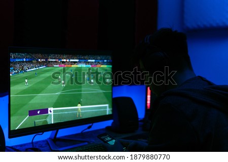 Young man is looking at his phone while playing football game. The room was illuminated with blue light. Royalty-Free Stock Photo #1879880770