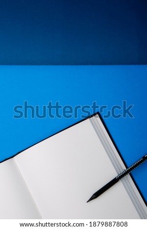 black color pencil on blank notebook on a blue background