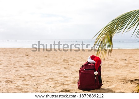 Santa Claus hat on backpack standing on sand beach. Christmas and New Year celebration. Nobody.