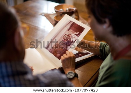 First point of view of a senior man and woman looking at a old wedding photo album. Remembering the past. Mature love. Top shot. Indoor, daytime.