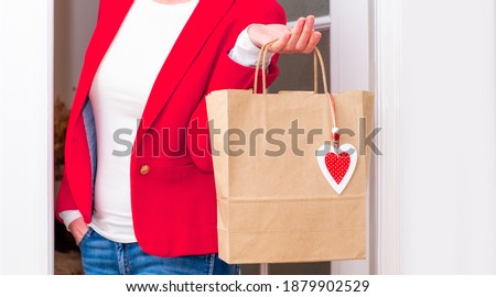 Woman's hands holding Shopping bag with red Hearts of Valentine's Day near the white door.