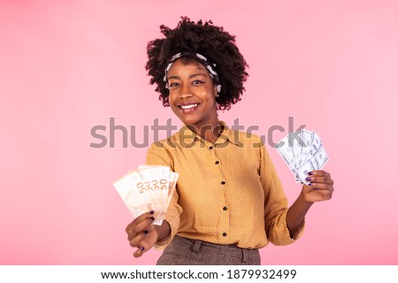 Portrait of a cheerful young woman holding money. African american woman smiling and holding euro and dollar bank notes, feeling happy and satisfied