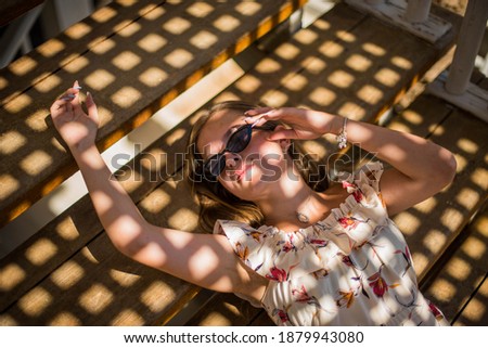 A fashion portrait of a beautiful young female girl wearing sunglasses relaxing on a stairs on a sunny summer day in cafe on the beach. young slim beautiful woman summer vacation, sunny.