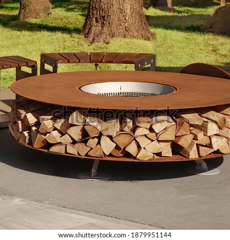 Round Patio Iron Fire Pit Table For Outdoor Leisure Party. Steel Rounded Fire Pit With Grill Top On Backyard Party Place. Grill Appliance And Fireplace On The Back Yard Lawn.