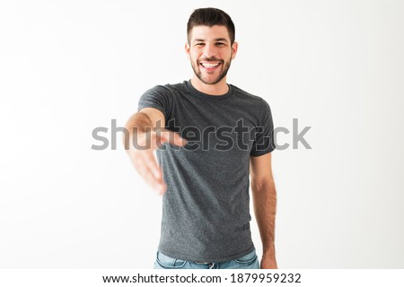Attractive man in his 20s is laughing with a big smile. Latin guy has his arm raised and is trying to reach and touch something in front of him Royalty-Free Stock Photo #1879959232