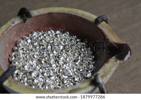 A ceramic crucible or melting pot with grains of sterling silver 925 for jewelry making after hand smelting in a workshop. One of the two major precious metals on the market. Royalty-Free Stock Photo #1879977286