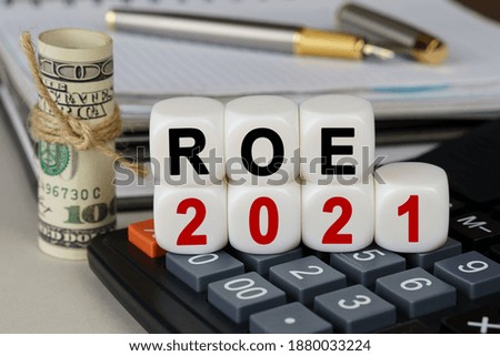 Business and finance concept. There are cubes on the calculator that say - ROE 2021. Nearby out of focus - dollars, notebook and pen