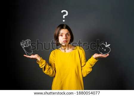 A young funny girl in a yellow sweater with a surprised expression is puzzled over what to eat. Thinks about the benefits of being a vegan, raw food and avoiding fatty, unhealthy junk food.