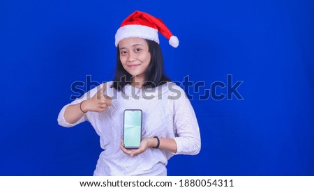 Asian woman wearing christmas hat holding green screen handphone isolated blue background