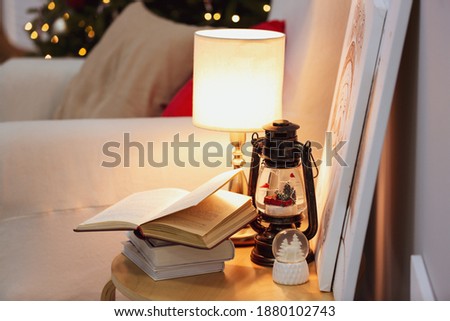 Books, snowglobes and lamp on wooden table in room. Christmas decor