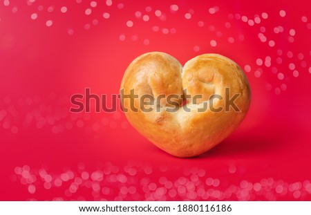 Romantic bread heart on red background with bokeh lights. Yeast bread bun shaped like a heart. Concept for valentines day or baking with love.Traditional Swiss butter bread called Zopf or Challah.