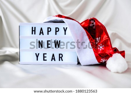 Lightbox with text HAPPY NEW YEAR with santa hat on silk fabric background. Winter holiday concept. Christmas and New Year