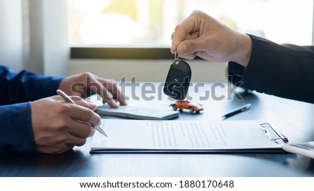 Hand holding car keys and car rental concept A close-up view of the agent, giving the customer the car keys after signing the lease, rental form and car name.