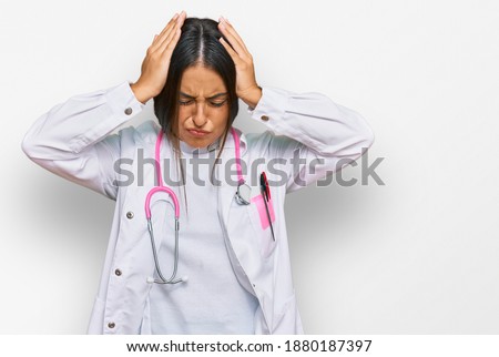 Beautiful hispanic woman wearing doctor uniform and stethoscope suffering from headache desperate and stressed because pain and migraine. hands on head. 