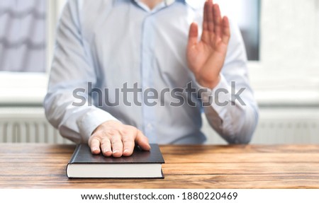 Oath. Witness. Closed Bible book on the table. The man holds his hand on the Bible. Oath concept with raised hand. Royalty-Free Stock Photo #1880220469