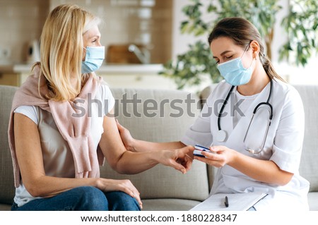 Homehealth care. Woman nurse in a medical mask help middle aged woman during during illness or pressure, female doctor measures the patient's pulse and oxygen saturation using a pulse oximeter Royalty-Free Stock Photo #1880228347