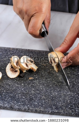 Slicing Champignon Mushroom using Sharp Knife on Black Marble Chopping Board. Cooking Process in the Kichen 