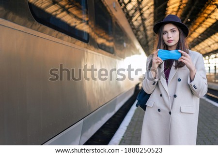 Female tourist at the railway station wearing on mask before entering of the train car. Pandemic concept