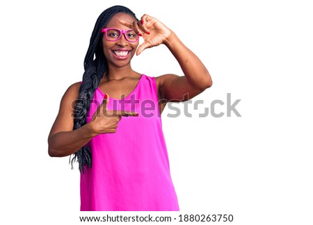 Young african american woman wearing casual clothes and glasses smiling making frame with hands and fingers with happy face. creativity and photography concept. 