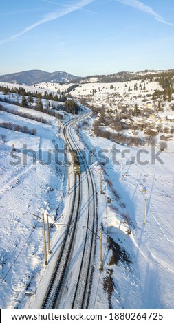 Train in the snowy mountains. The mountain pass, covered with snow and the railway track on the edge of the mountain, aerial photo in winter. Route of passenger and freight trains. Vertical photo