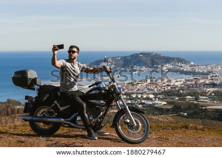 Biker sitting on the motorcycle taking selfie with the landscape with the mobile