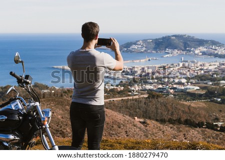 Biker standing taking photo of the landscape with the mobile
