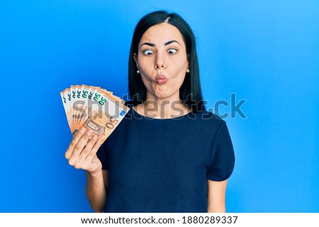 Beautiful young woman holding bunch of 50 euro banknotes making fish face with lips, crazy and comical gesture. funny expression. 