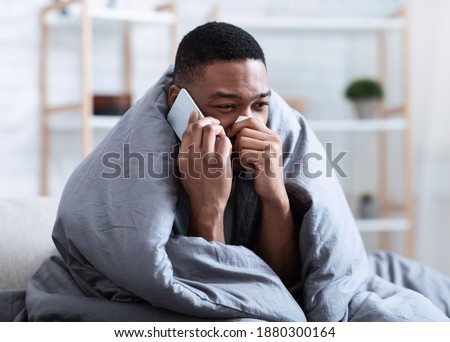 Ill Black Man Calling Doctor Having Runny Nose Suffering From Cold And Rhinitis Sitting On Sofa At Home. Sick African Guy Talking On Phone Feeling Unwell. Symptoms. Influenza Symptoms Royalty-Free Stock Photo #1880300164