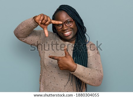 Young black woman with braids wearing casual clothes and glasses smiling making frame with hands and fingers with happy face. creativity and photography concept. 