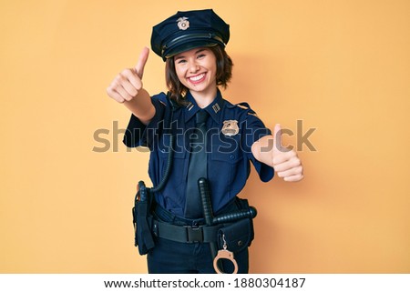 Young beautiful woman wearing police uniform approving doing positive gesture with hand, thumbs up smiling and happy for success. winner gesture. 