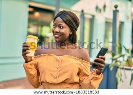 Young african american woman using smartphone drinking coffee at the city.