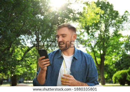 Young man with refreshing drink and smartphone in park