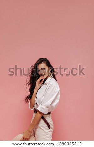 Photo of wonderful woman with curly long brunette hair in stylish light cloth and unusual earrings on isolated background..