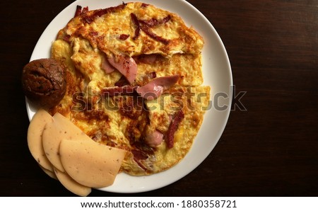top view of a dark wooden surface with a large white platter with a variation of a cooked breakfast of fried eggs and sausage with cheese chunks and a round rye bun plus copy space to the right