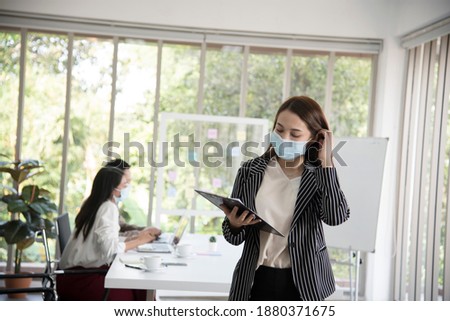 Asian female office worker wears hygienic mask on her face at work to protect from coronavirus or Covid-19. Concept for New normal lifestyle at work. Awareness of wearing facemask.Soft focus
