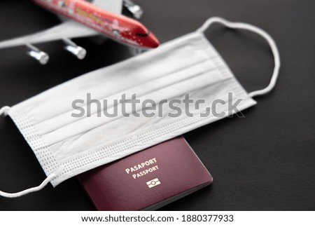 Safe travel during the virus covid-19 pandemic . Airplane model with face mask, passport, isolated on black background, top view. Nobody, no people, space for text on left side, Selective focus. 