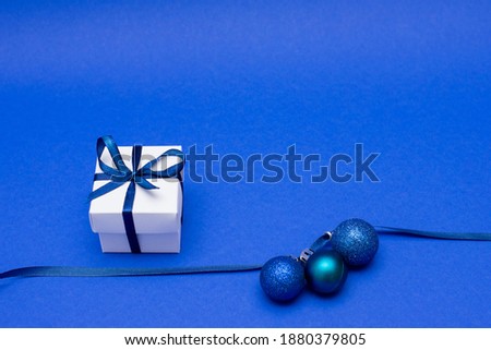 white surprise gift box with ribbon and christmas decorations on blue background, copy space