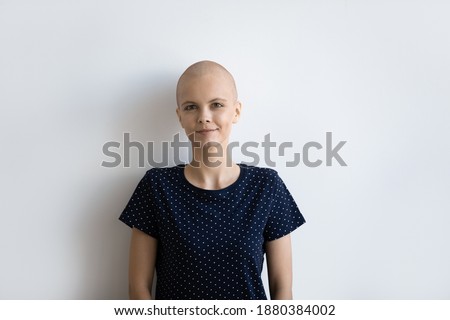 Head shot portrait of smiling confident young woman having oncology posing at studio isolated on white background. Optimistic sick hairless female looking at camera motivated on struggle with cancer